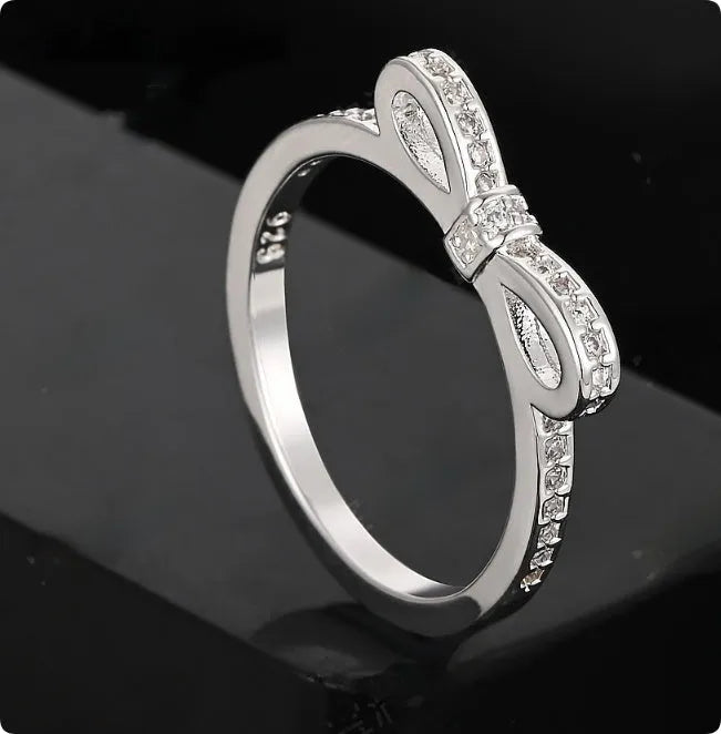 Silver bow-shaped ring with sparkling zircon crystal stones on a finger.