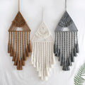 Handwoven triangle dream catcher pendant in brown with cotton web, iron ring, wooden beads, and tassel on a light wall