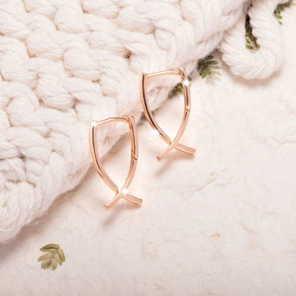 Rose gold cross shaped earrings with copper construction on display card