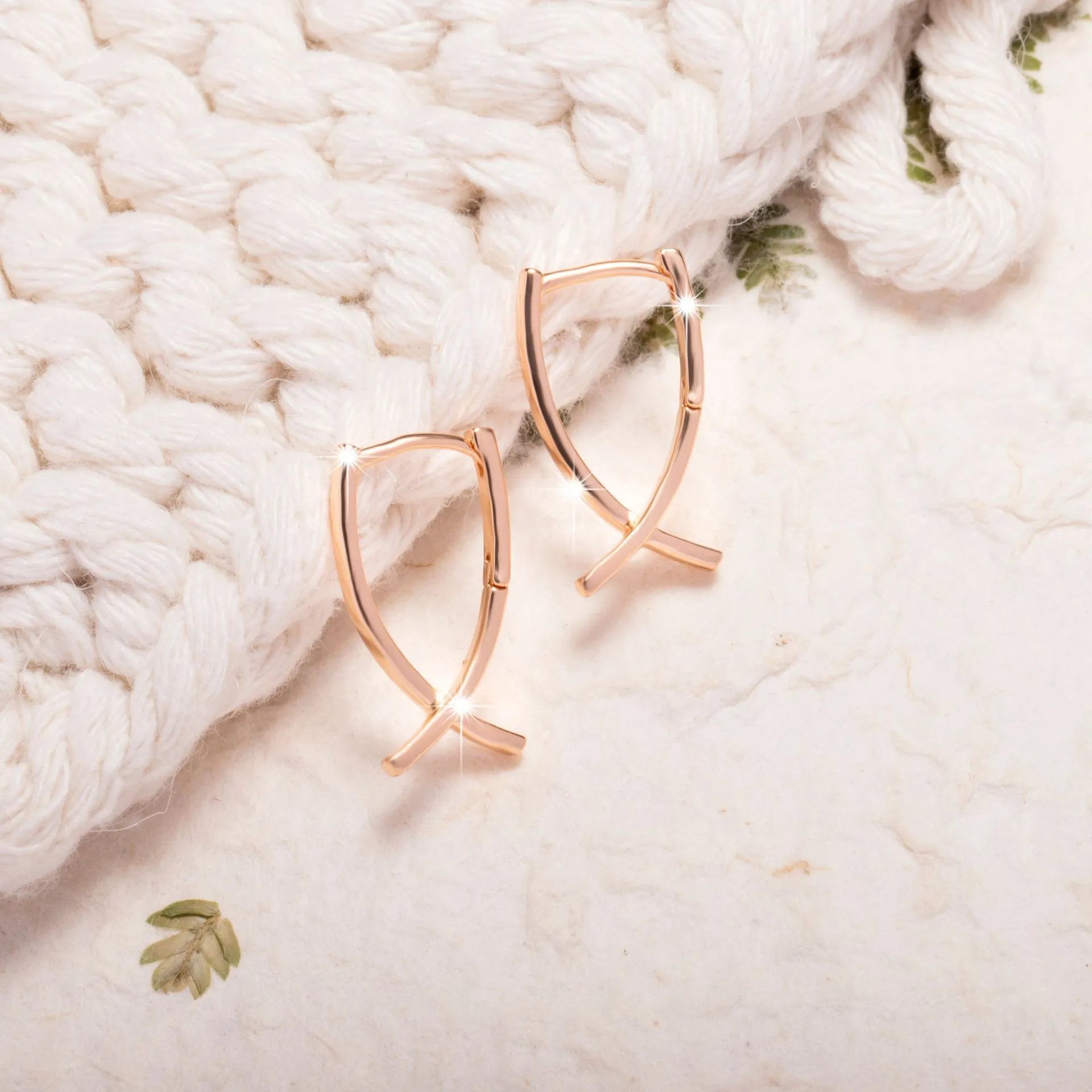 Rose gold cross shaped earrings with copper construction on display card