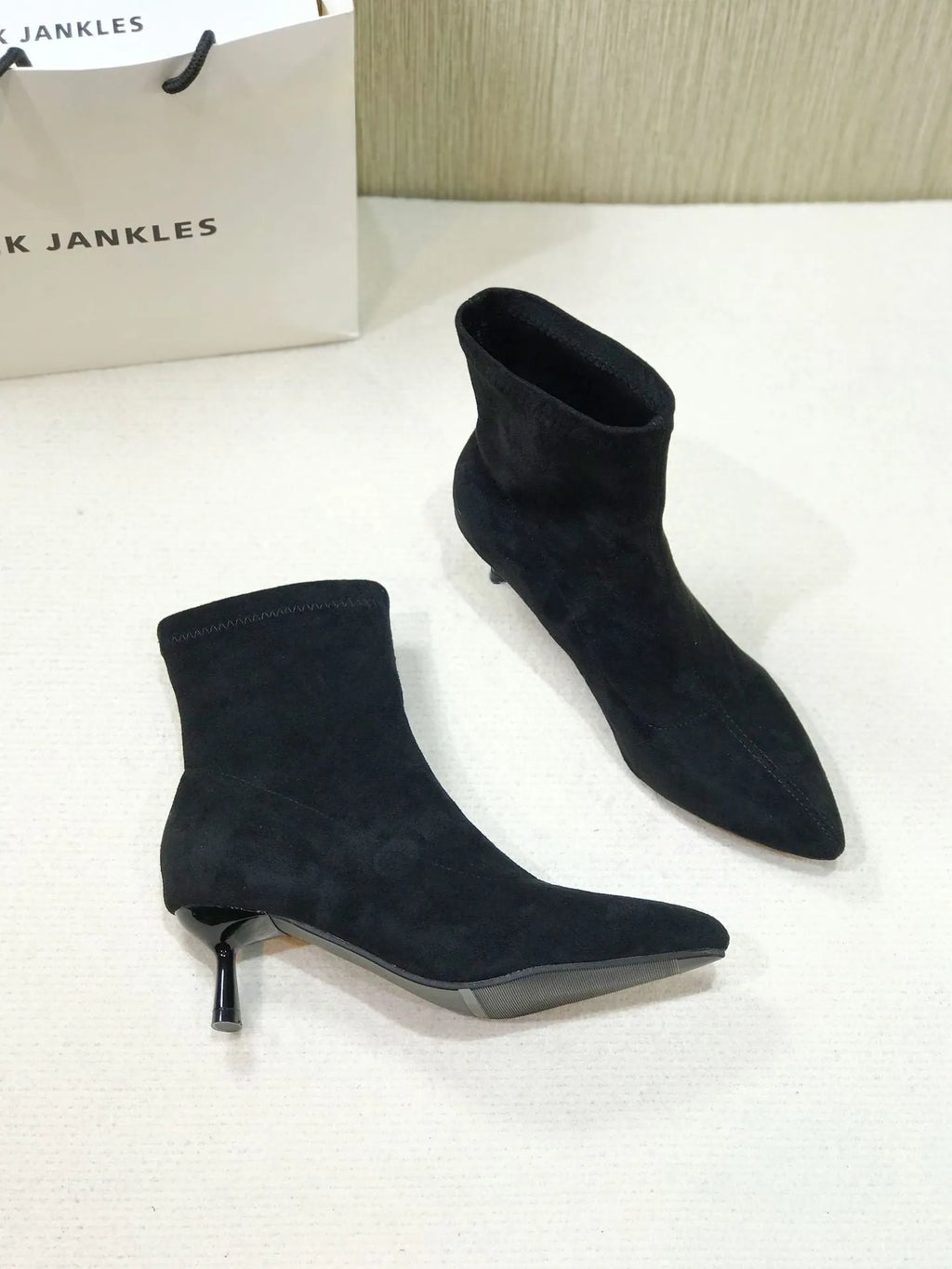 Black pointed toe women's ankle boot with high stiletto heel and mid-calf shaft on a plain background.