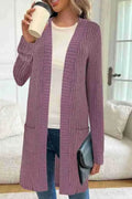 Woman wearing a loose grey long sleeve knitted cardigan jacket with pockets.