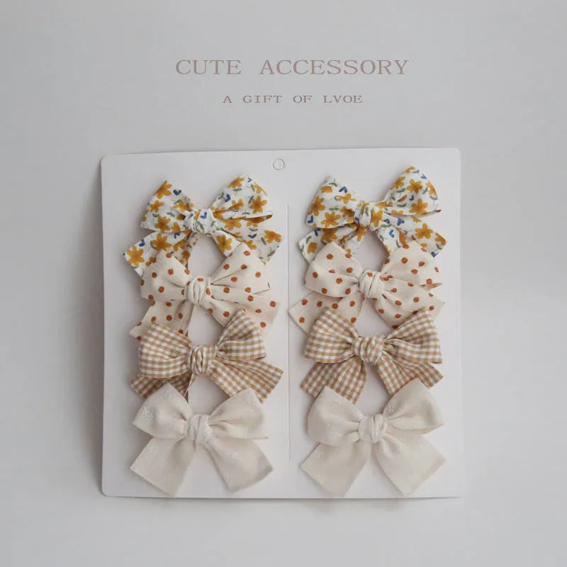 Set of fabric dovetail bow hair clips for children in various colours including beige, pink, and blue flowers.