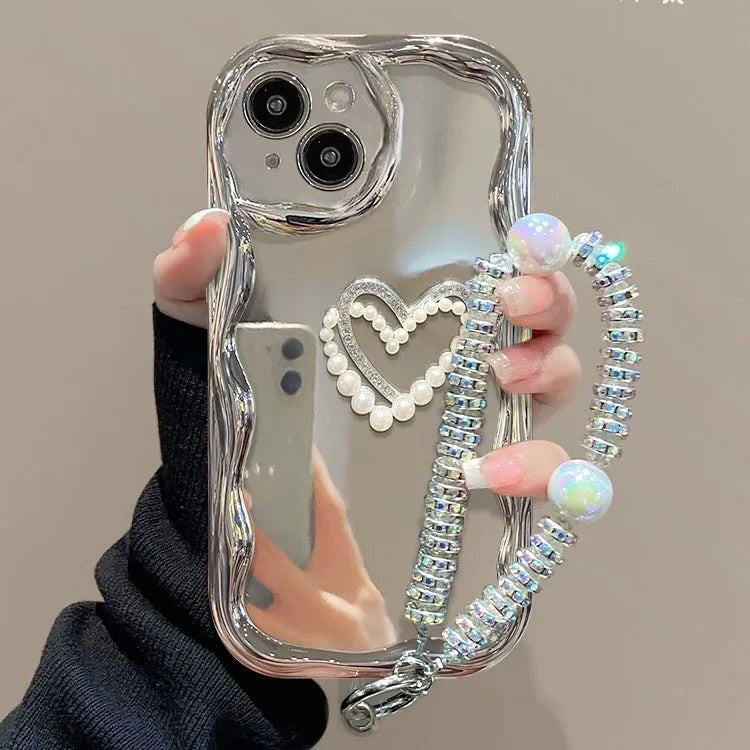 Silver grey silicone phone case for iPhone 15 Pro Max with three-dimensional pearls and chain, electroplated finish, and matching bracelet on a table