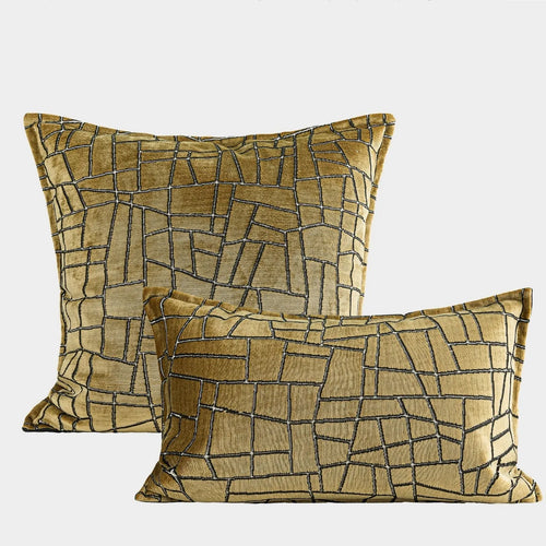 Gold geometric abstract patterned square cushion on a grey sofa.