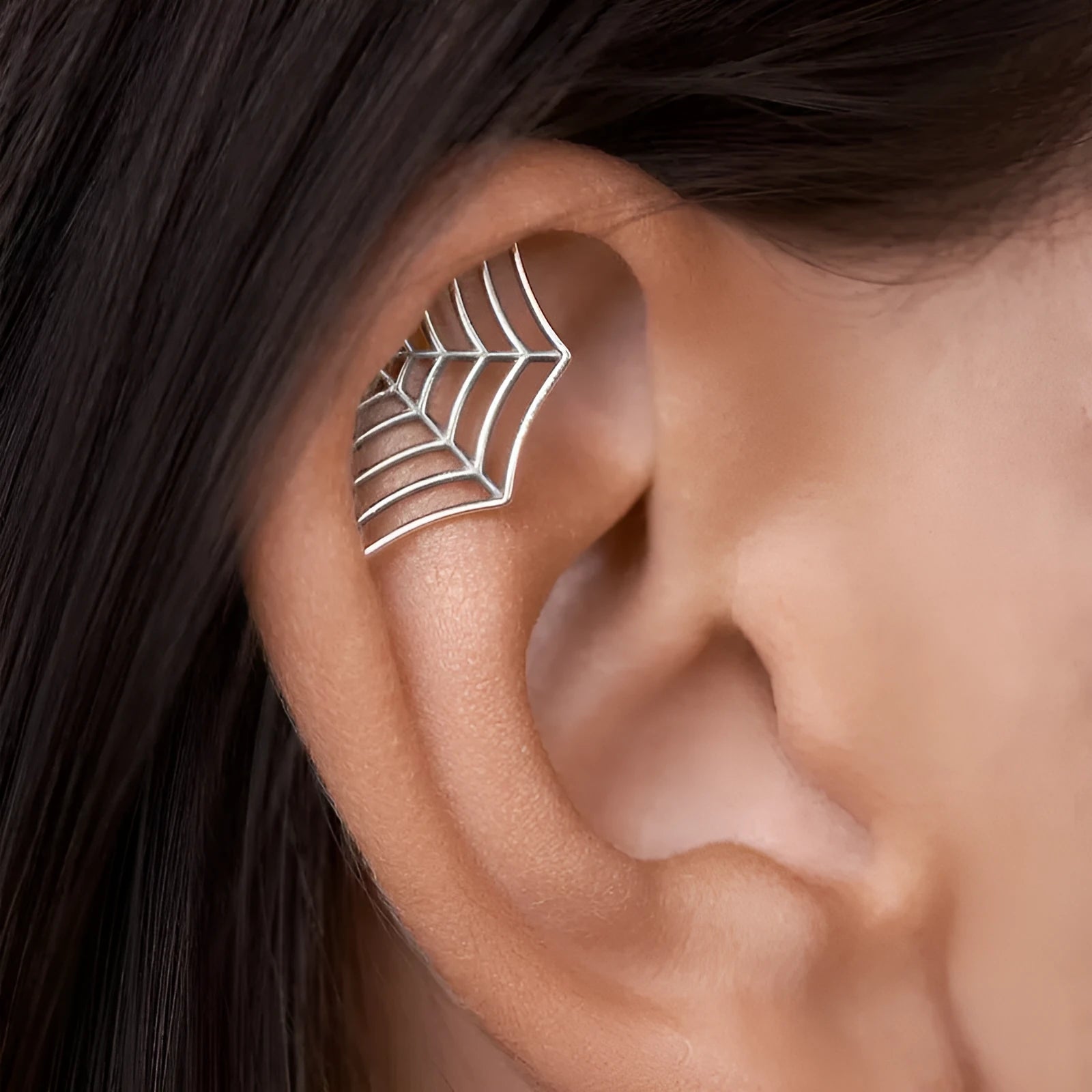 Close-up of geometric spider web patterned metal stud earrings in a gold electroplated finish.