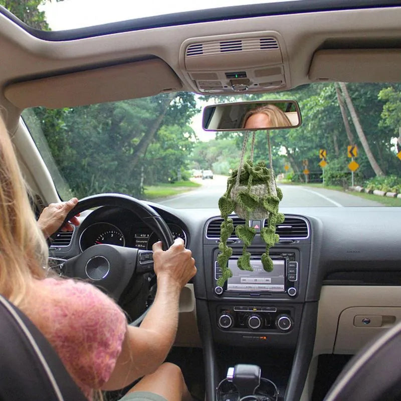 Green and white crocheted car plant decoration with hanging rope on a car dashboard.