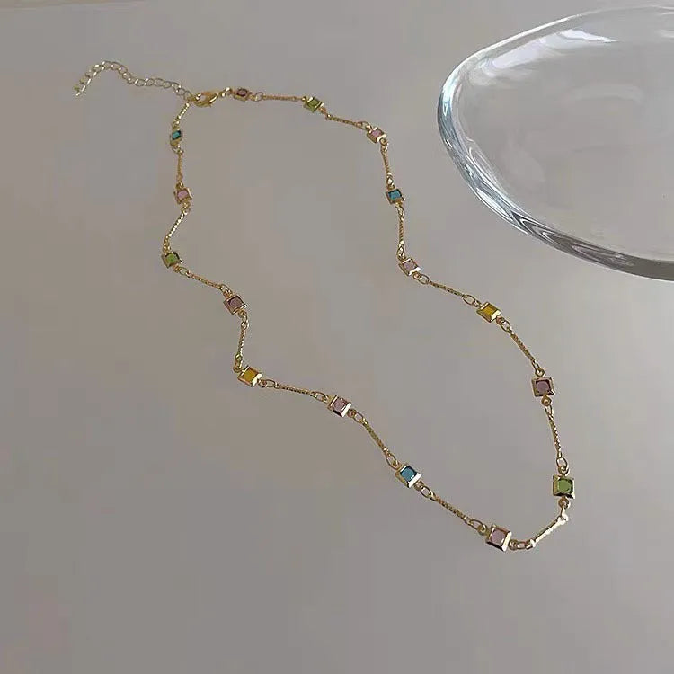 Square geometric clavicle chain necklace in gold tone with artificial crystal details on a white background.