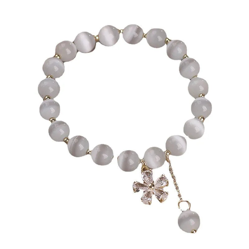 White cat's eye crystal women's bracelet with safety buckle pendant and small flower tassel on a single loop.