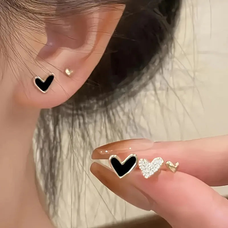 Three pairs of heart-shaped alloy earrings in gold, black, black and white, and pink colours with electroplated finish