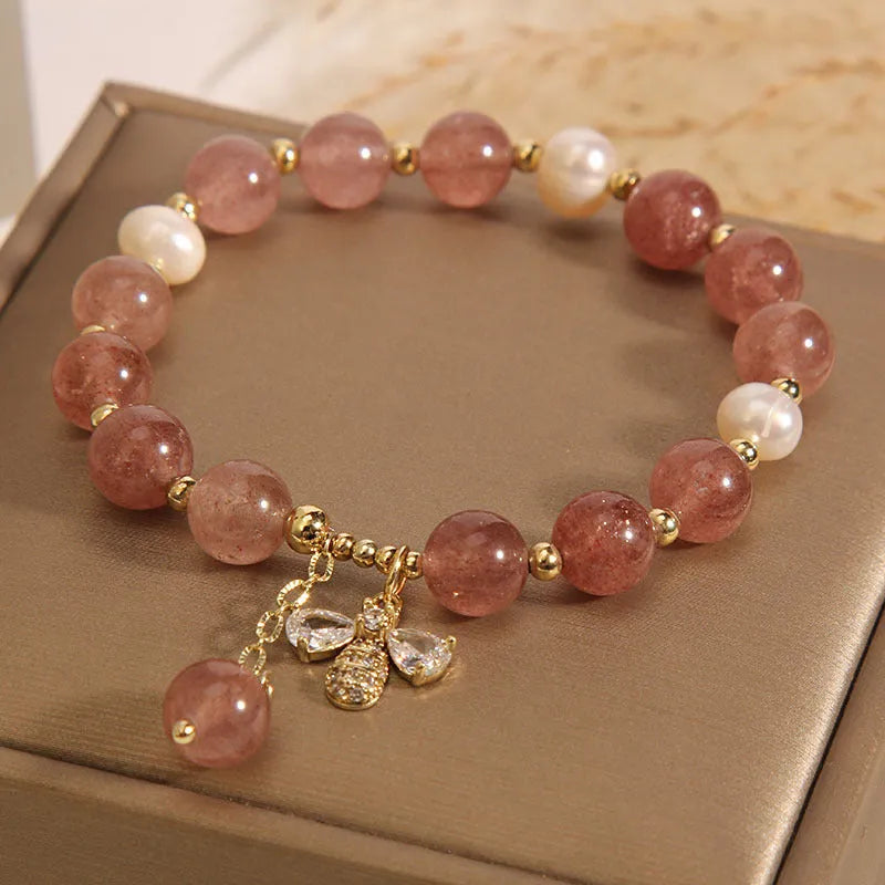Women's pink strawberry quartz and white freshwater pearl bracelet with zircon details on wrist.