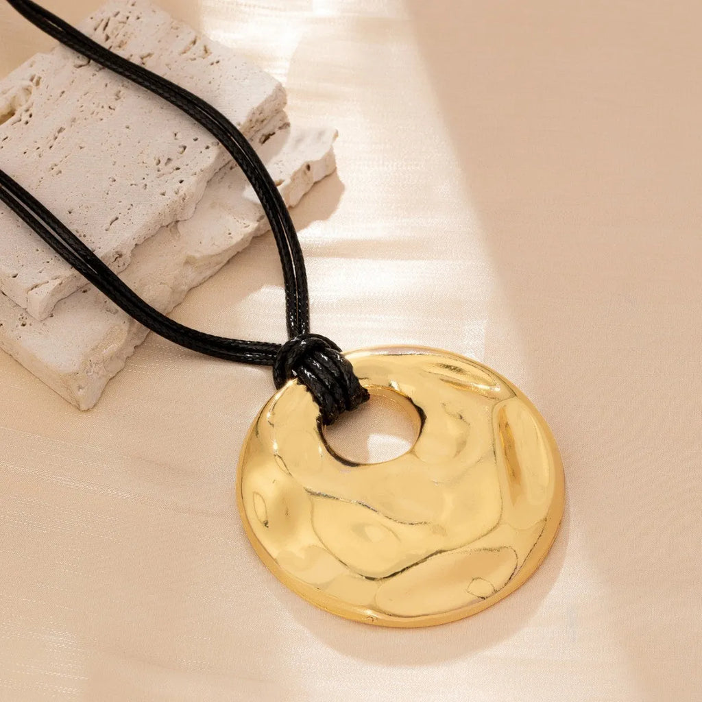 Women's gold alloy oval pendant necklace with braided rope chain on a plain background