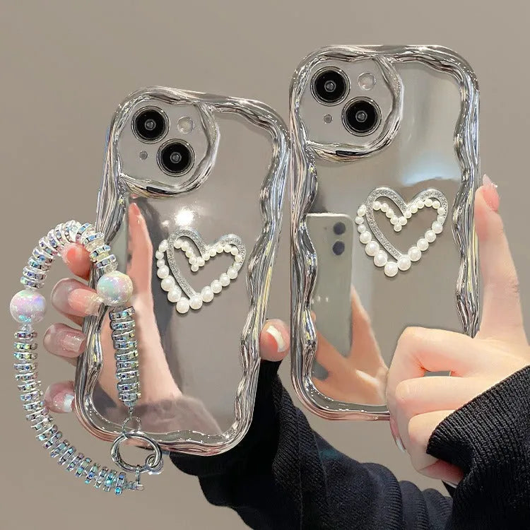 Silver grey silicone phone case for iPhone 15 Pro Max with three-dimensional pearls and chain, electroplated finish, and matching bracelet on a table