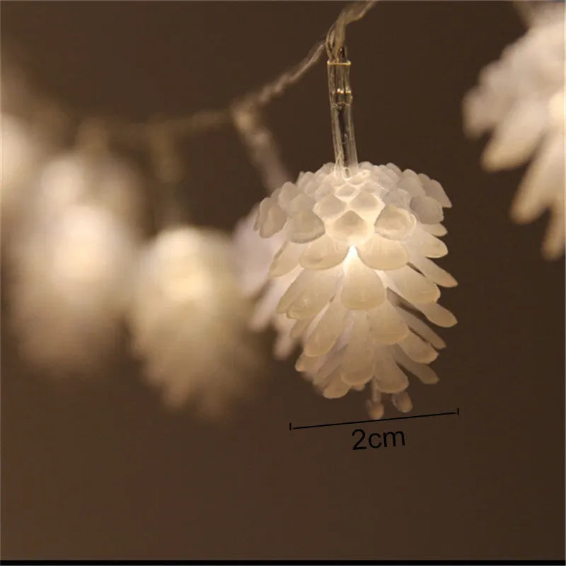 Warm white LED pine cone string lights draped over a surface, showing plastic shell details and battery pack.