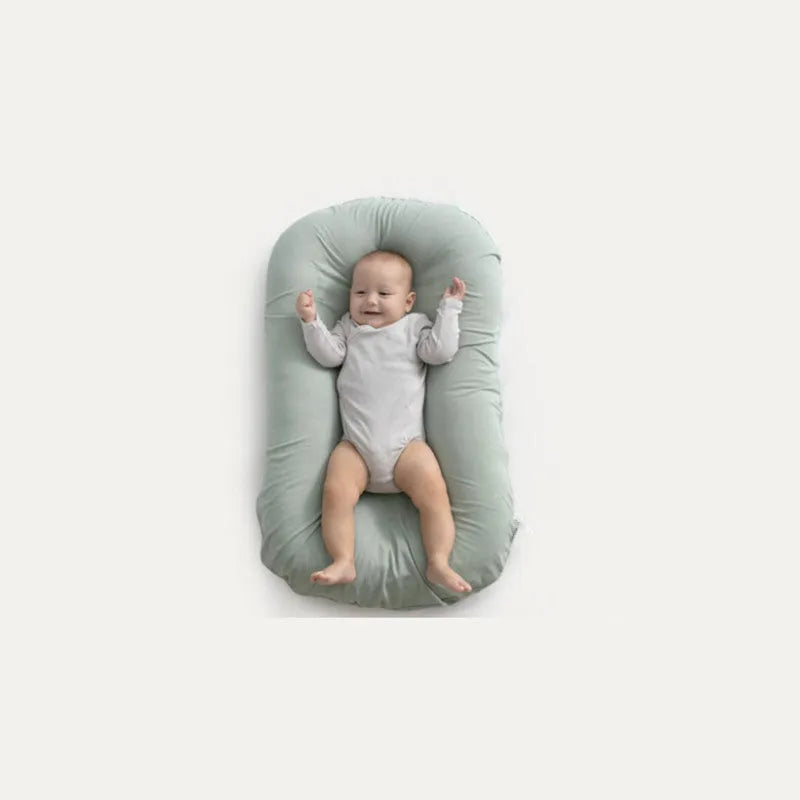 Beige portable baby nest crib cot for newborns on a neutral background.