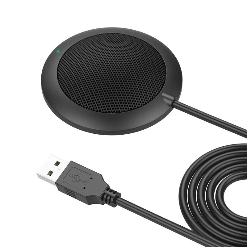 Black USB desktop microphone with metal mesh cover on a desk next to a laptop
