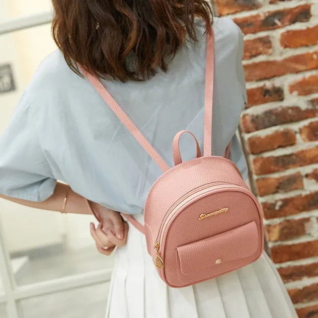 Small black women's backpack shoulder bag with zipper closure shown next to a mobile phone for scale