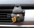 Black and white resin fortune cat ornament designed to clip onto a car air vent as an aromatherapy diffuser.