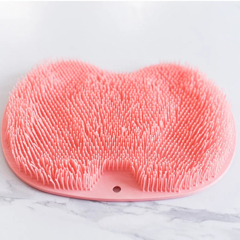 Orange silicone suction cup bath brush mat with bristles for foot and back cleaning on a bathroom floor.