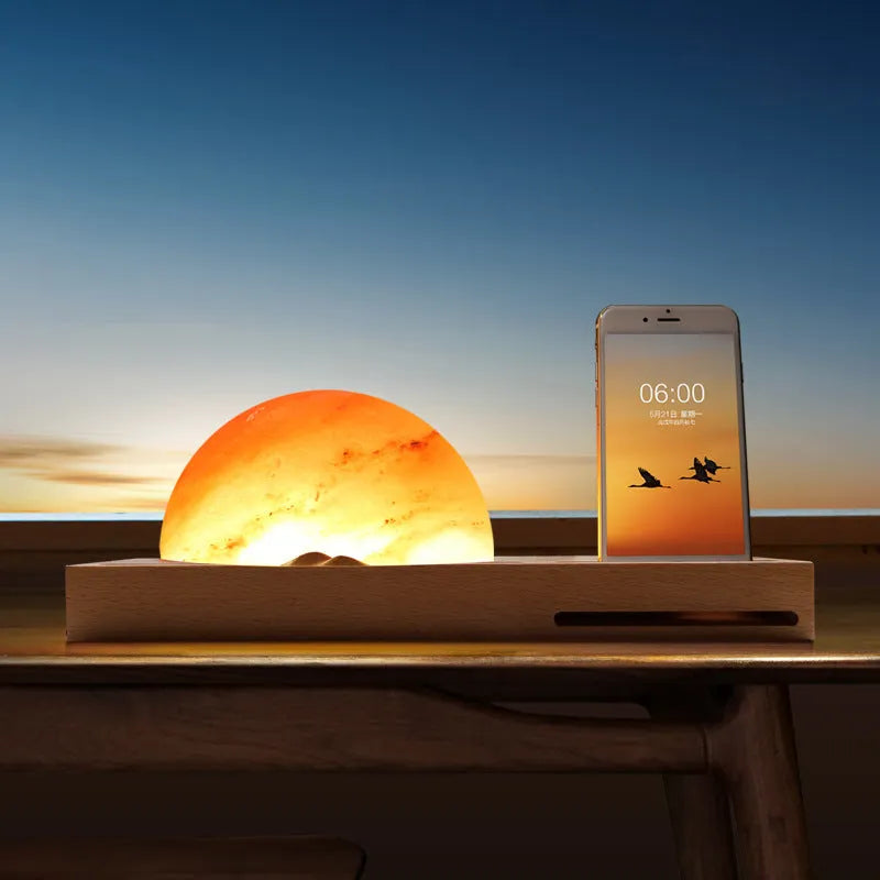 Wooden-based table lamp with a glowing orange Himalayan salt shade, wirelessly charging a mobile phone on its surface.