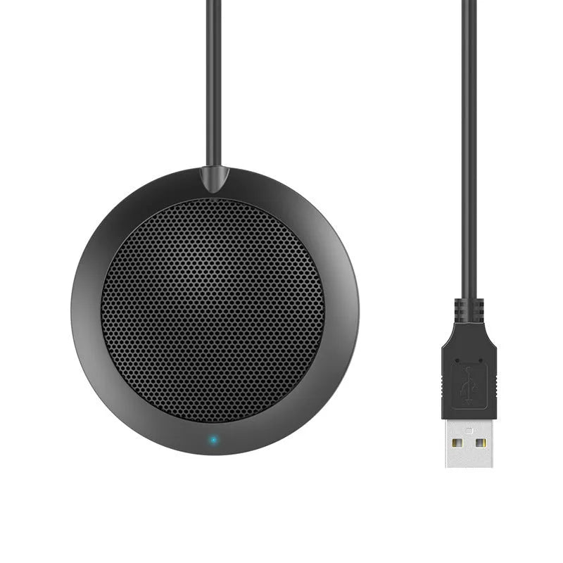 Black USB desktop microphone with metal mesh cover on a desk next to a laptop