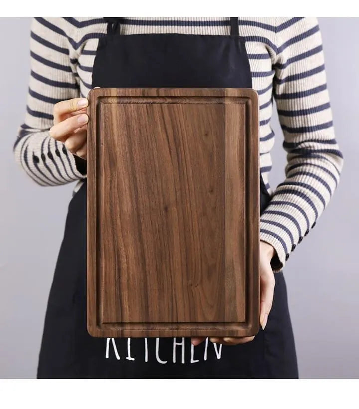 Black walnut wood cutting board with sauce groove and carved side handle on kitchen counter