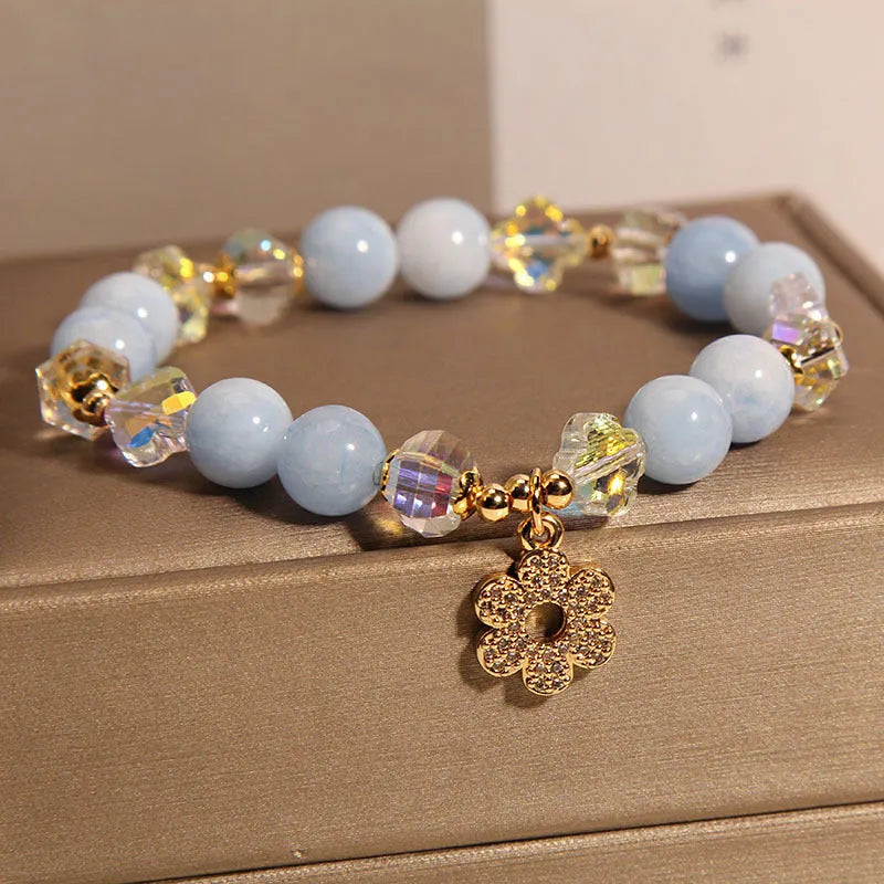Aquamarine crystal bracelet with four-leaf clover charm and pearl detail on a wrist.