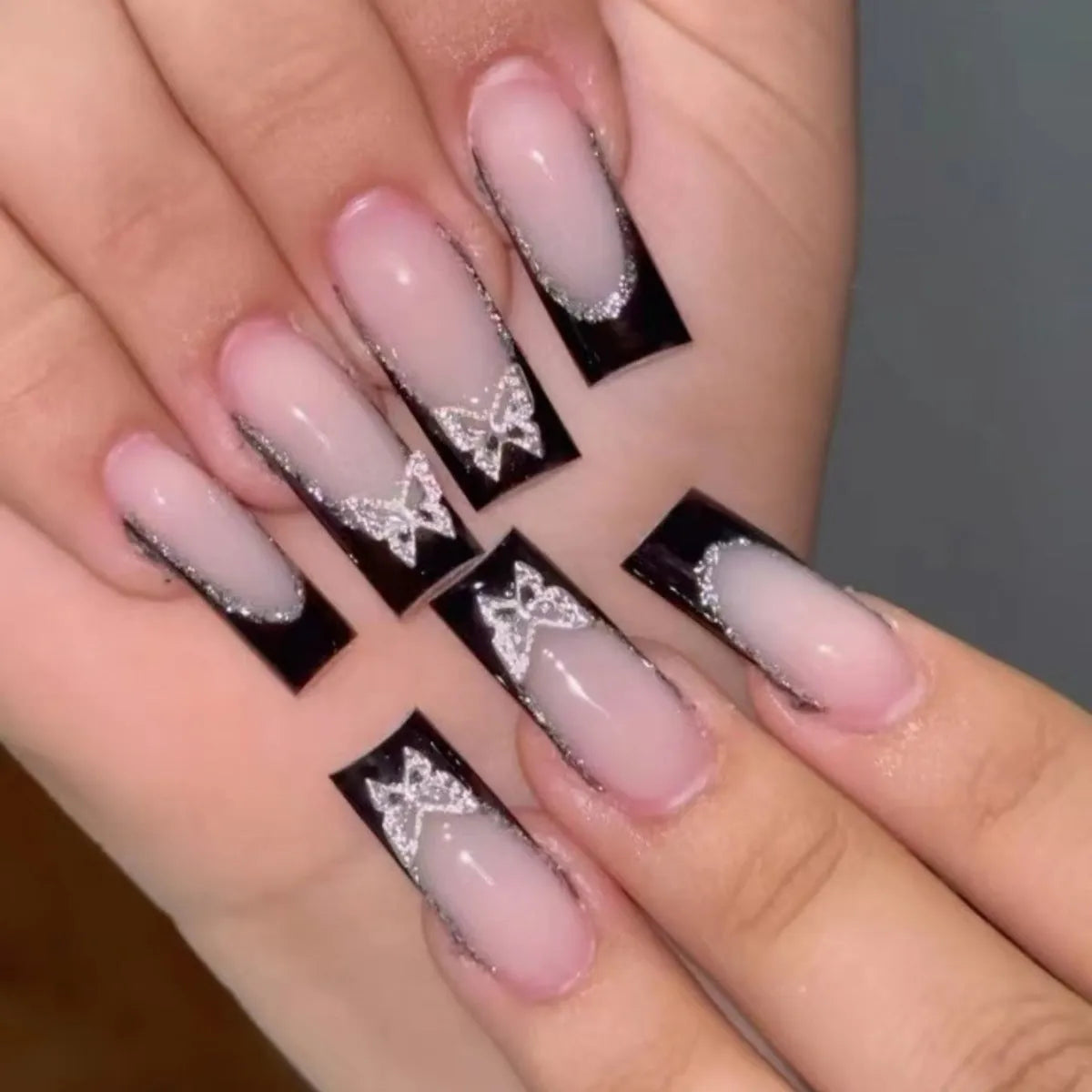 French-style false nails with glittering butterfly design in medium length with jelly glue adhesive