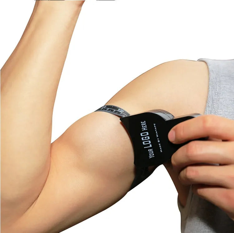 Black ABS plastic body fat caliper skinfold tester with measuring tape on a grey background.