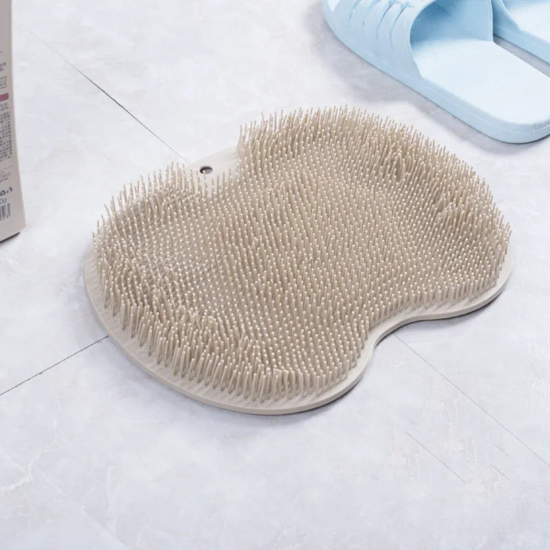 Orange silicone suction cup bath brush mat with bristles for foot and back cleaning on a bathroom floor.