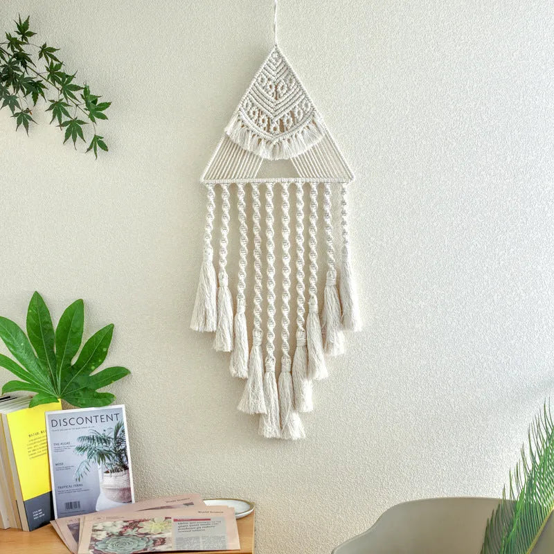 Handwoven triangle dream catcher pendant in brown with cotton web, iron ring, wooden beads, and tassel on a light wall