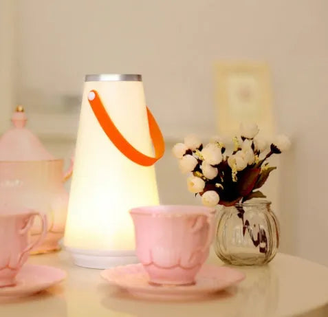 White rechargeable LED bedside lantern with USB cable on a table.