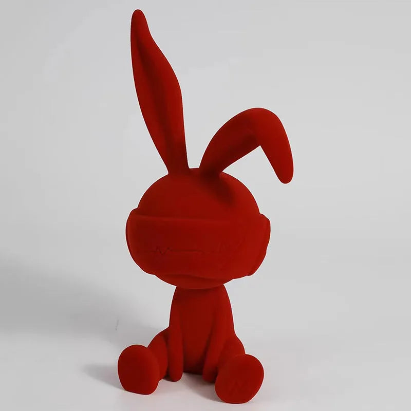 Small resin rabbit ornament wearing a suede blindfold, shown in blue, green, and red colour options.