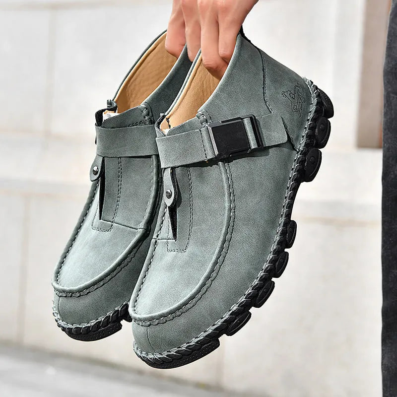 Men's black handmade stitching slip-on loafers with a flat heel on a wooden floor.