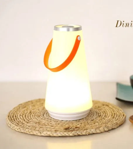 White rechargeable LED bedside lantern with USB cable on a table.