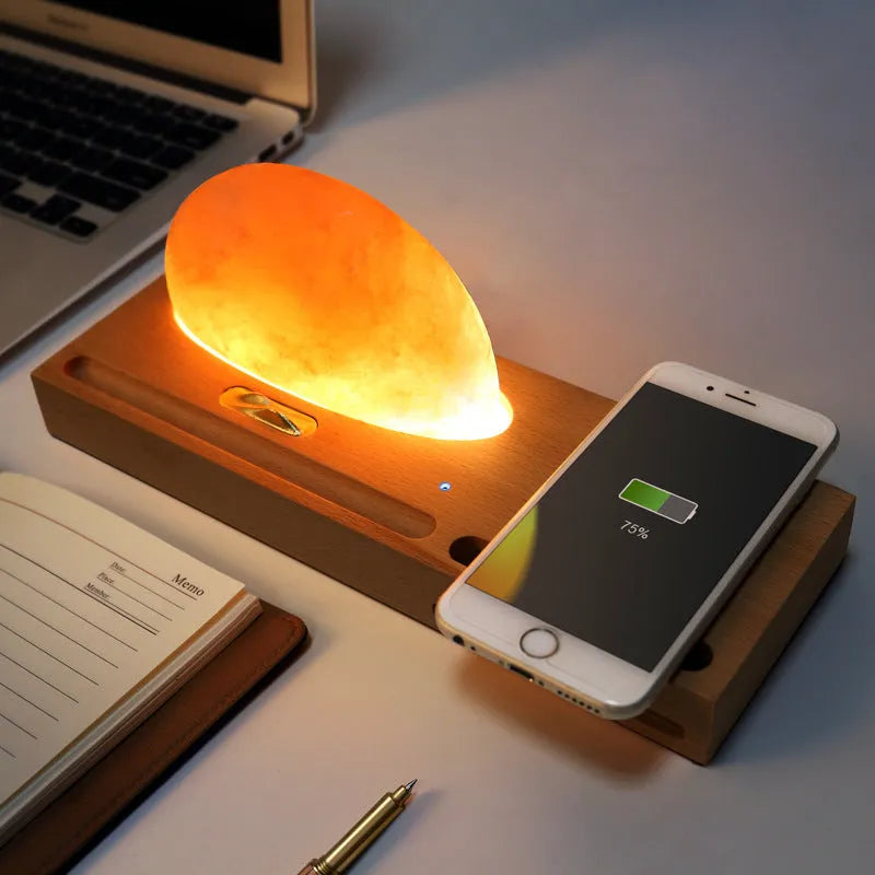 Wooden-based table lamp with a glowing orange Himalayan salt shade, wirelessly charging a mobile phone on its surface.