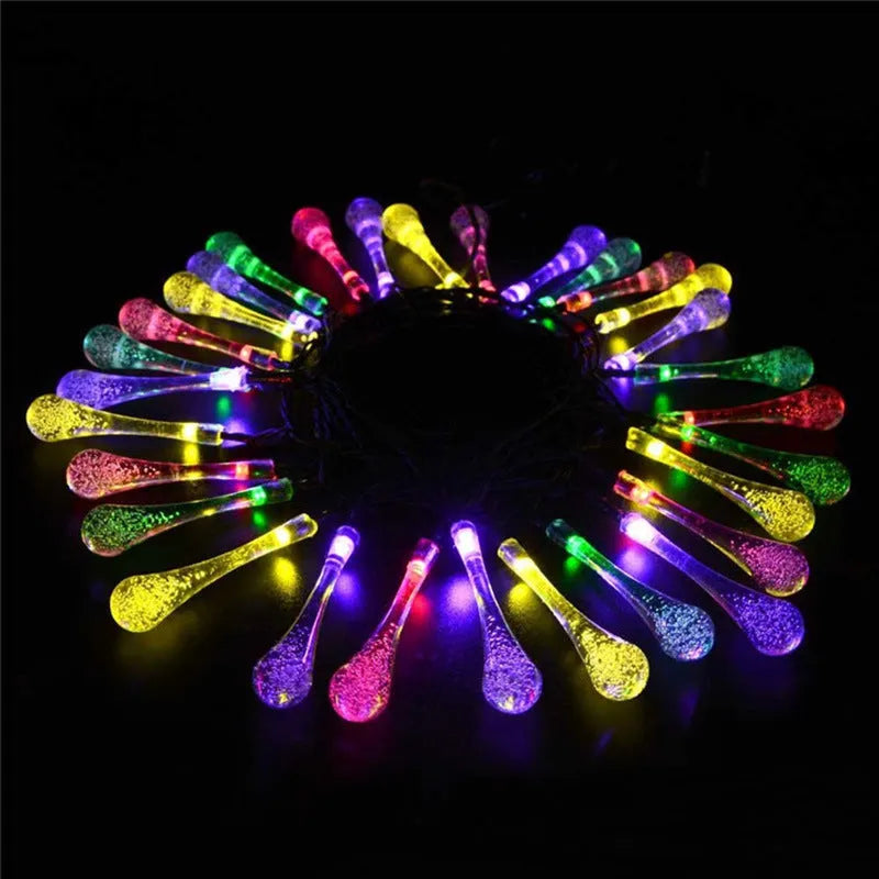 String of solar-powered bubble drop LED lights with a solar panel and ground spike for outdoor garden use.