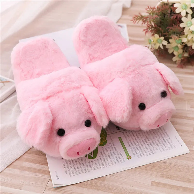 Pink pig-shaped plush floor slippers on a clean floor, showing the short plush fabric and pig design details.