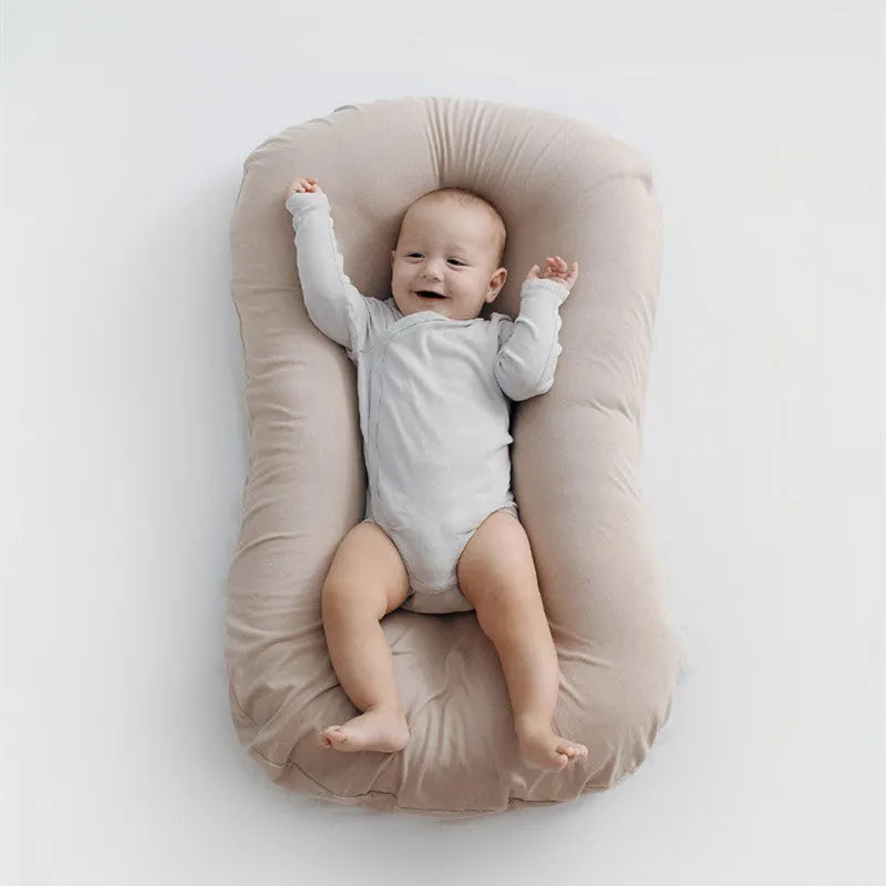 Beige portable baby nest crib cot for newborns on a neutral background.