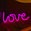 Pink love-shaped LED neon sign light with flexible silicone shell on a table.