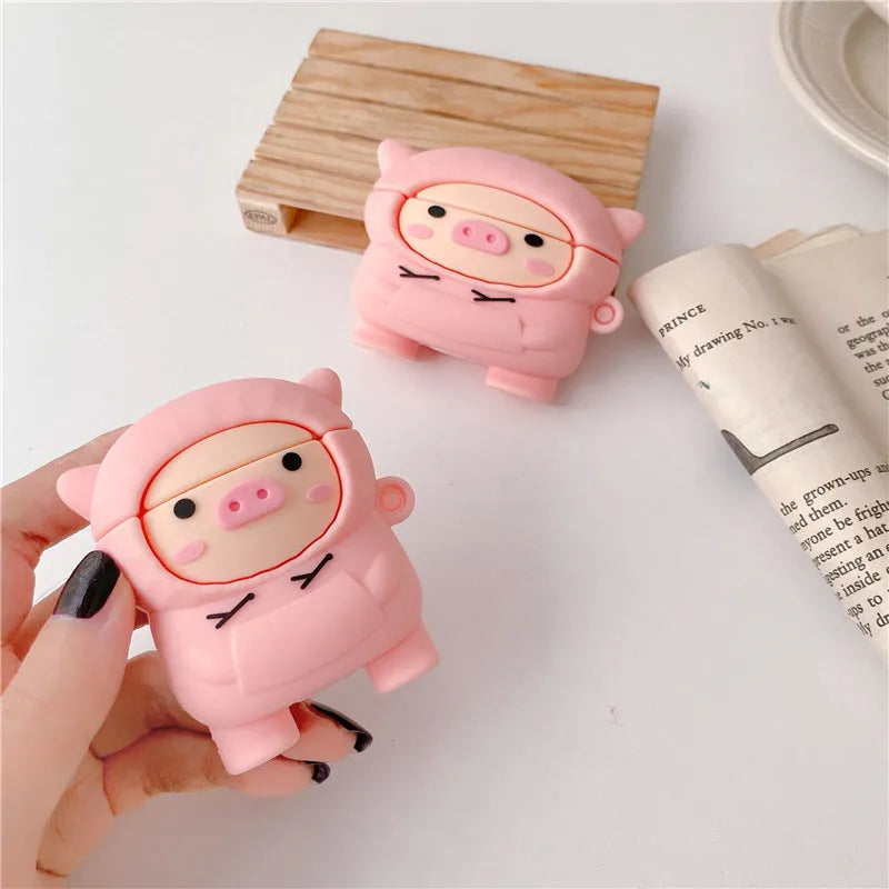 Pink silicone AirPods case with a cartoon pig in a sweater design and a silver keychain hook attached.