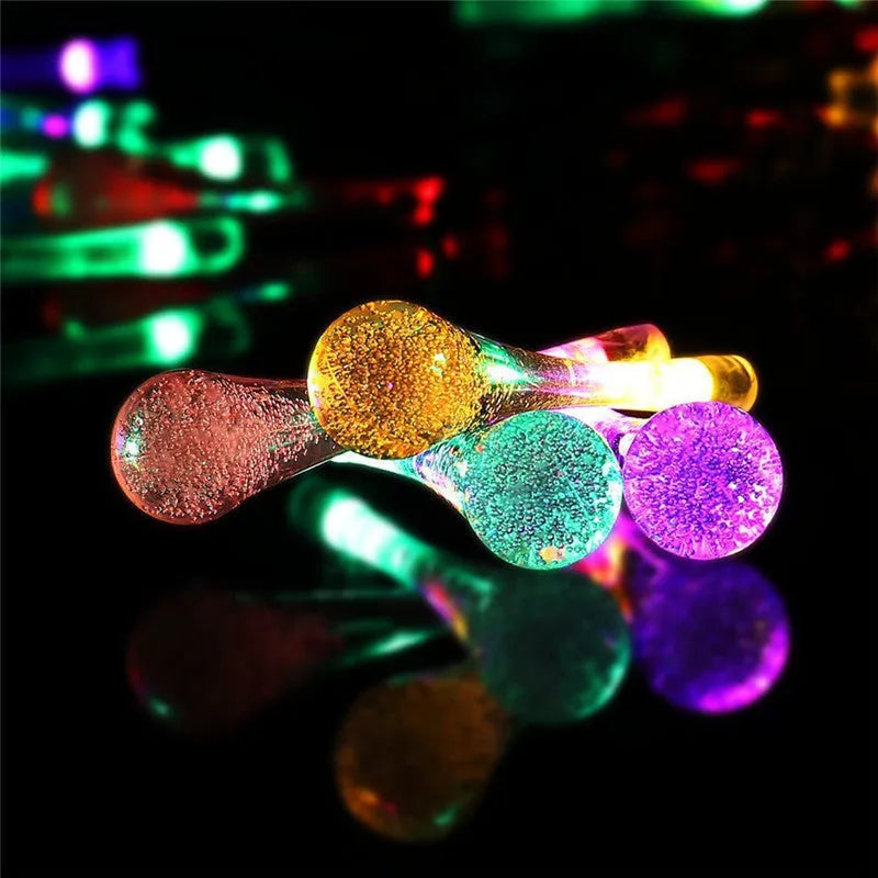 String of solar-powered bubble drop LED lights with a solar panel and ground spike for outdoor garden use.