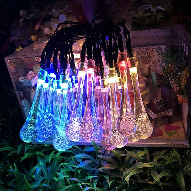 String of solar-powered bubble drop LED lights with a solar panel and ground spike for outdoor garden use.