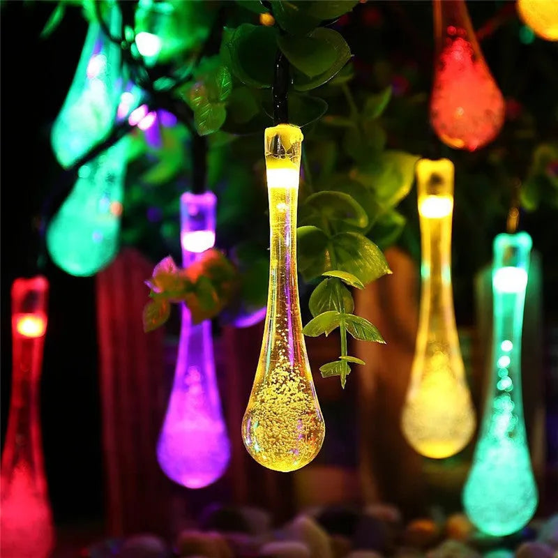 String of solar-powered bubble drop LED lights with a solar panel and ground spike for outdoor garden use.