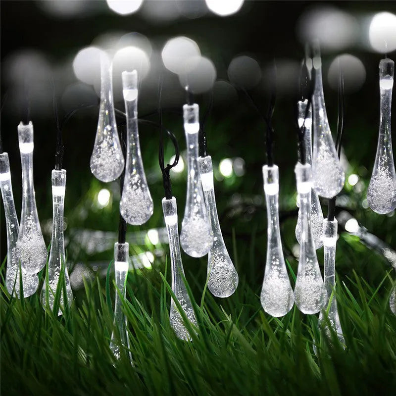 String of solar-powered bubble drop LED lights with a solar panel and ground spike for outdoor garden use.