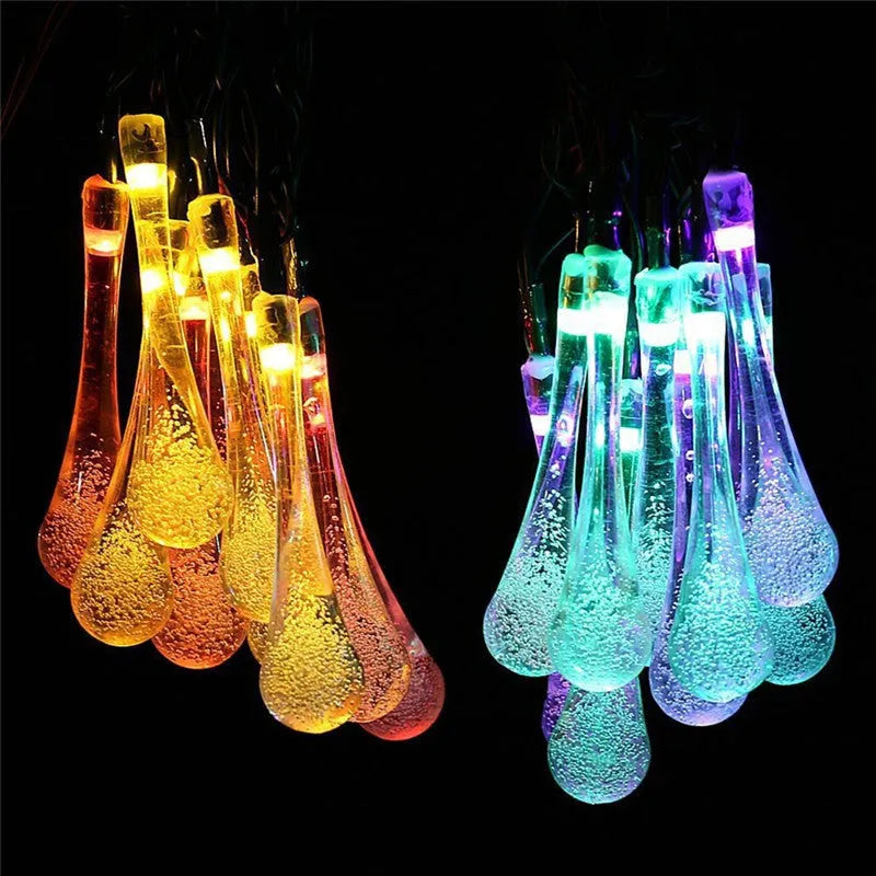 String of solar-powered bubble drop LED lights with a solar panel and ground spike for outdoor garden use.