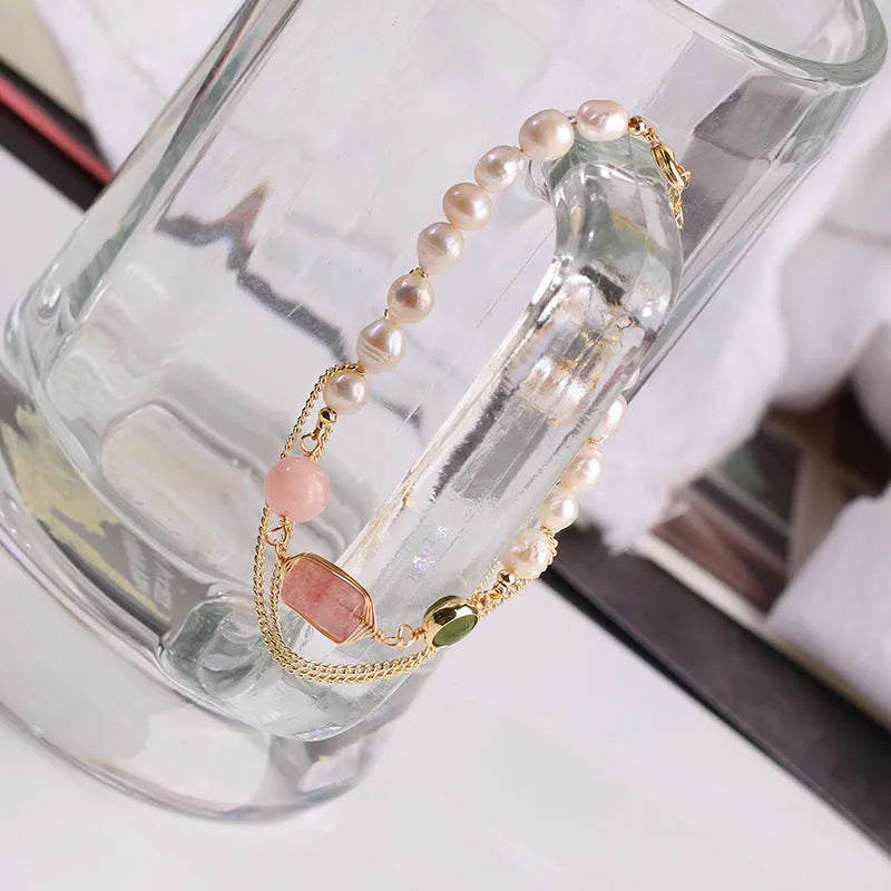 Close-up of a pink freshwater pearl bracelet with strawberry-shaped crystal charms on a geometric model.