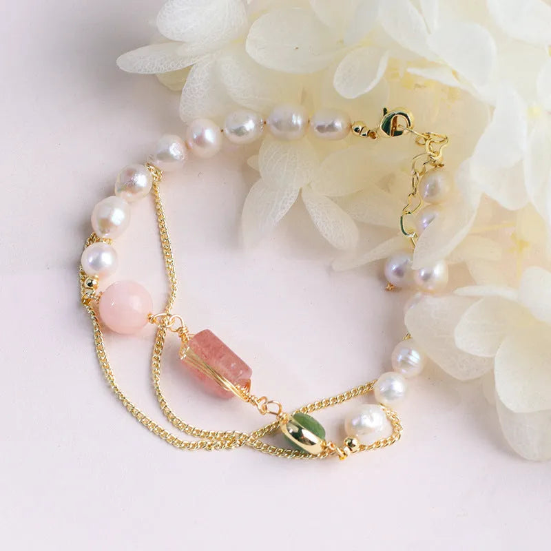 Close-up of a pink freshwater pearl bracelet with strawberry-shaped crystal charms on a geometric model.