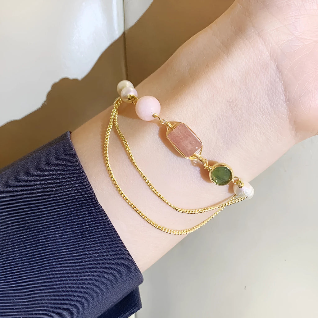Close-up of a pink freshwater pearl bracelet with strawberry-shaped crystal charms on a geometric model.