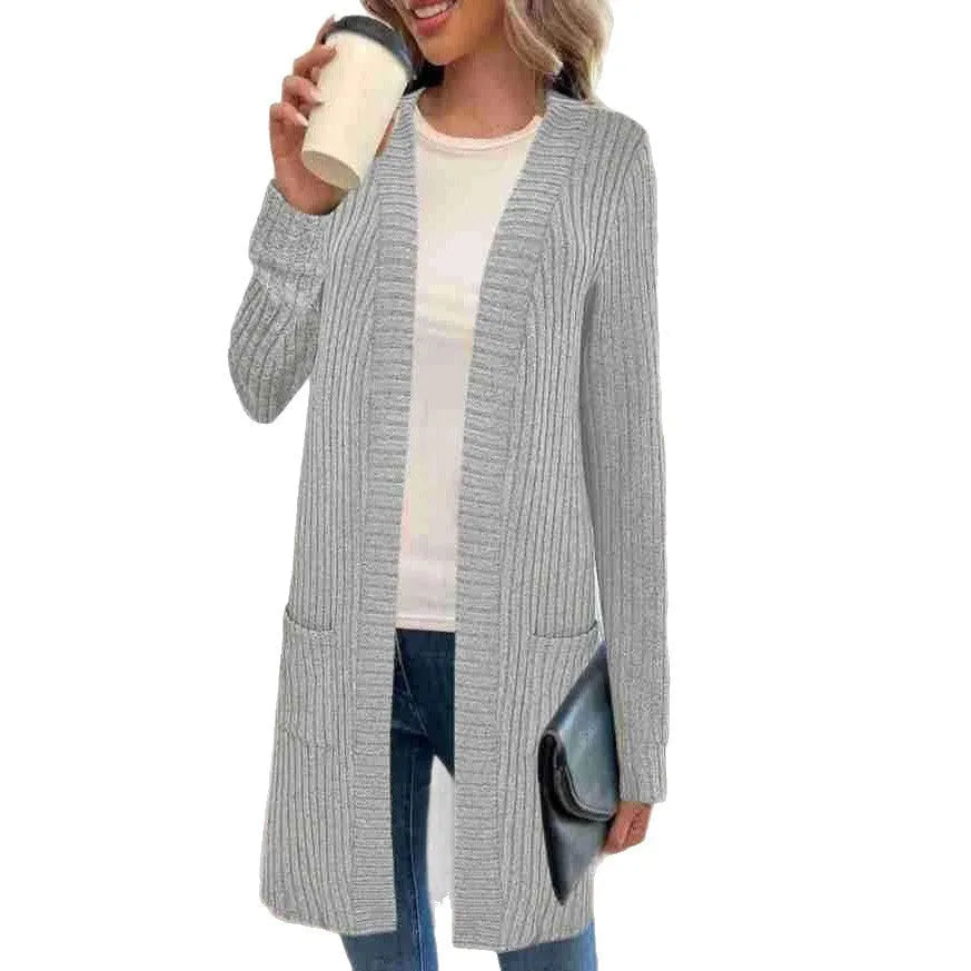 Woman wearing a loose grey long sleeve knitted cardigan jacket with pockets.